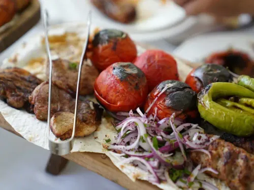 A plate of mixed kebab served with charred tomatoes and onions on flat bread