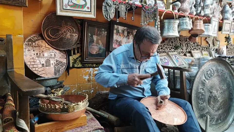 A master copper artisan hand hammering patterns on a copper platter in Gaziantep