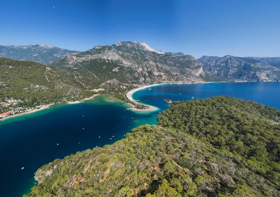 A hiker looking down at the turquoise waters of the Mediterranean sea along a rocky cliff path of the Lycian Way