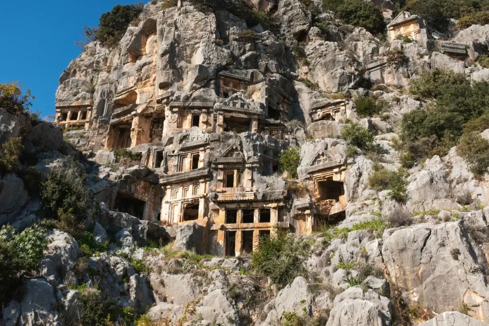 Ancient rock cut Lycian tombs carved directly into a steep cliff face along the hiking trail