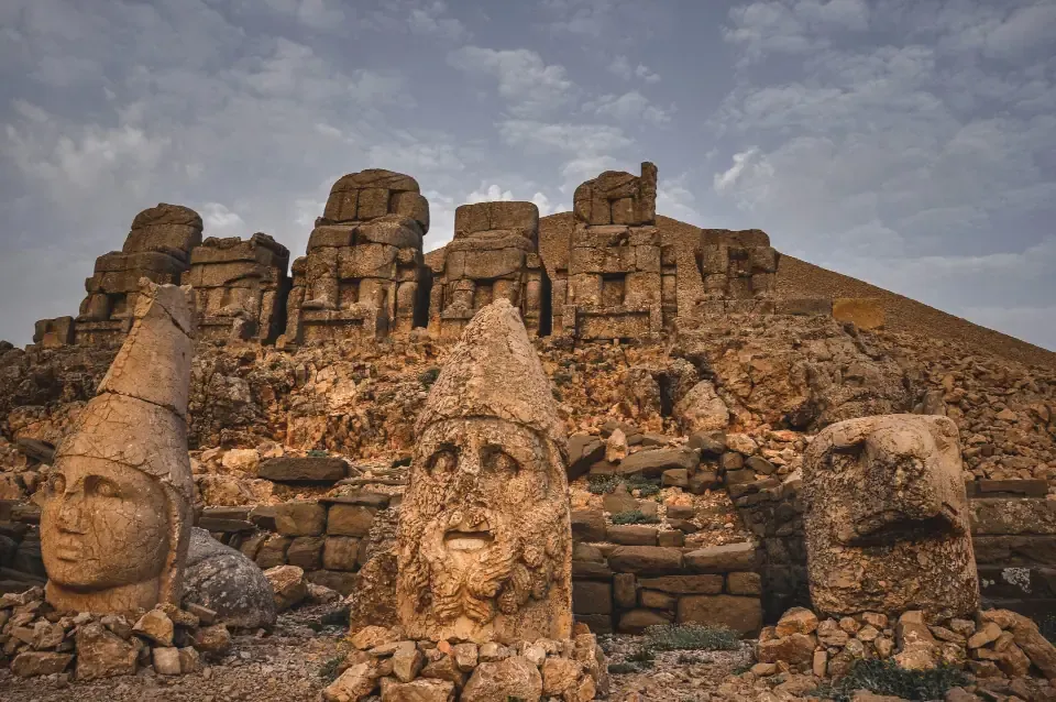 Row of massive stone heads of gods sitting on the mountain terrace overlooking mountain valleys