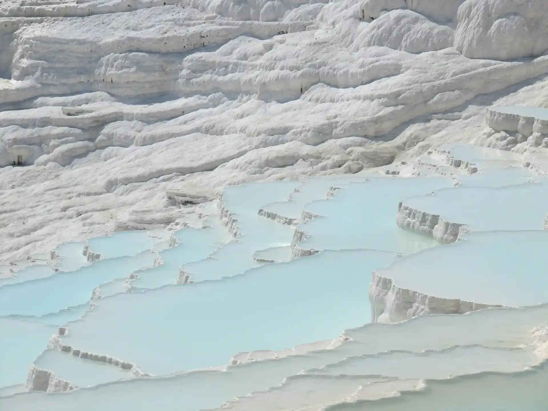 The stark white calcium travertine terraces and blue thermal pools of Pamukkale