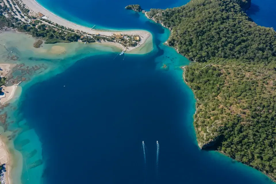 An aerial view from a paraglider looking down at the sweeping curved white sand spit of the Oludeniz Blue Lagoon